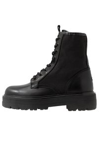 Schwarzer Knöchelstiefel mit einem strukturierten Obermaterial aus Stoff und glatten Lederelementen. Verfügt über Metallösen und eine robuste Gummisohle für besseren Halt.