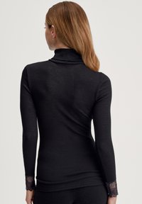 Zwarte geribbelde coltrui met lange mouwen, voorzien van kanten accenten bij de manchetten. Effen textuur en nauwsluitend ontwerp.