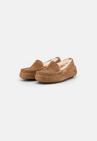 Bruine suède moccasin slippers met een zachte voering, decoratieve stiknaad en een merkaanduiding aan de zijkant, met een ronde teenontwerp.