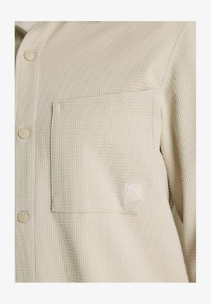 Svetlo bež srajca na gumbe iz teksturirane tkanine, s samim žepom na prsih in majhno logotipno značko.