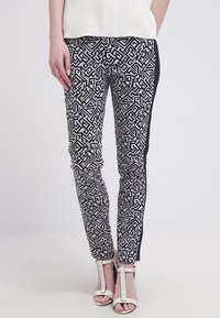 Svartvita mönstrade byxor med geometriska mönster, slim fit, med en enhetlig svart sidpanel, kombinerat med remmar i vitt på klackarna.