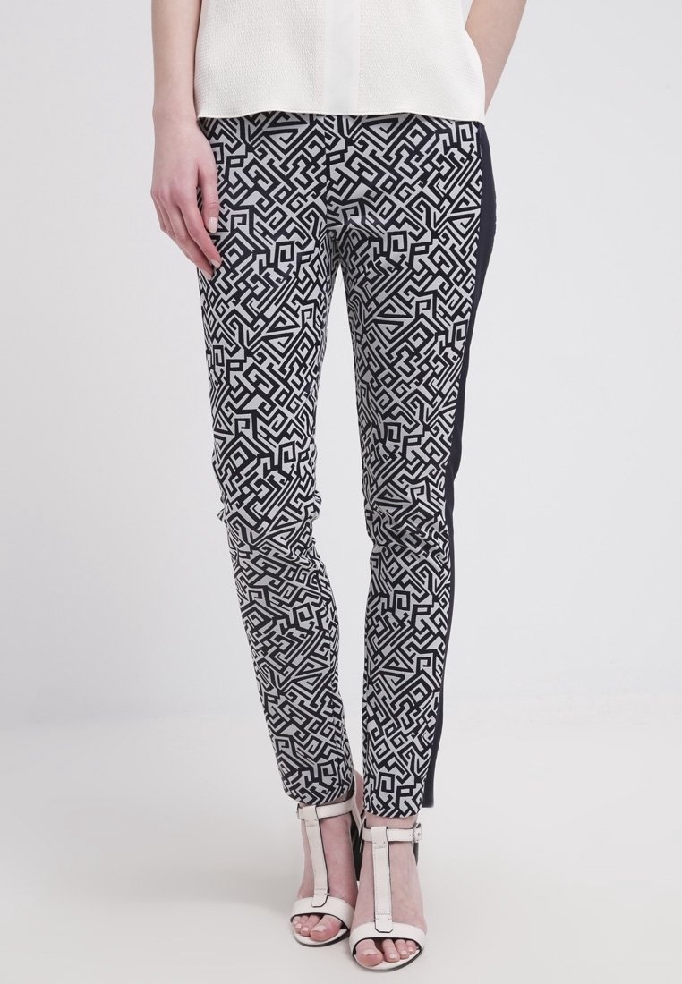Svartvita mönstrade byxor med geometriska mönster, slim fit, med en enhetlig svart sidpanel, kombinerat med remmar i vitt på klackarna.