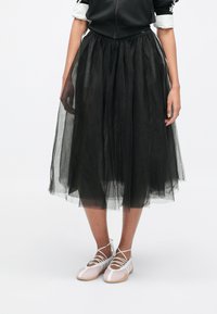 Čierna tylová sukňa s nariaseným pásom, s dĺžkou po stred lýtok. Kombinovaná s ružovými topánkami s bielymi remienkami a béžovou podrážkou.