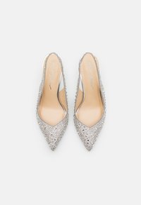 Escarpins argentés à bride, avec un bout pointu, recouverts de strass. Intérieur lisse avec un rembourrage minimal et logo de la marque en écriture métallique.