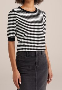 Haut en tricot à rayures noir et blanc avec des manches courtes et un col rond, associé à une jupe en denim noire avec des poches avant.