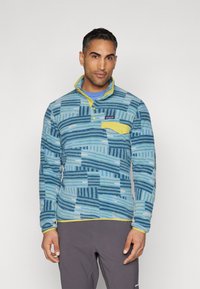 Fleece pulover s plavim i tirkiznim apstraktnim uzorkom, žutim ovratnikom i akcentima na džepu, te dizajnom s polu-molom. Mekana tekstura i toplo.