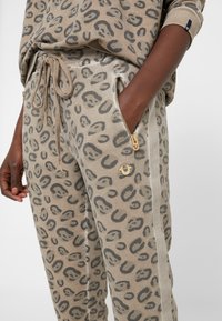 Leopardmuster-Jogginghosen in Beige und Grau, mit vorderen Reißverschlusstaschen mit goldfarbener Hardware und einem Kordelzugbund, aus weichem Stoff gefertigt.