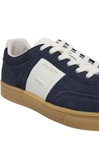 Mornarske suknje od semiša s bijelim kožnim naglascima, sadrže istaknuti "H" logotip, kremaste vezice i smeđu gumenu potplate s teksturiranim detaljima.