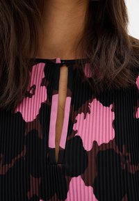 Svart och rosa veckad klänning med blommönster, med en nyckelhålsringning och en dekorativ knytning vid halsen.