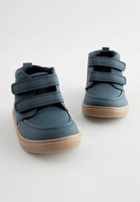 Niebieskie, wysokie buty sportowe z dwoma czarnymi paskami na rzepy, syntetyczna cholewka, zaokrąglony czubek i jasnobrązowa gumowa podeszwa; wyściółka z miękkiego materiału.