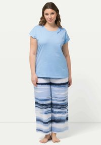 Ljusblå bomullströja med korta ärmar och broderad text "Good Vibes", tillsammans med vida byxor i blå och vita ränder.