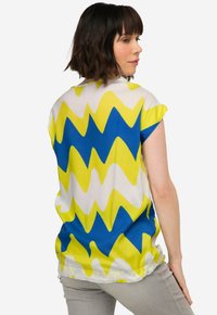 Kortærmet bluse med zigzag-mønster i gul, blå og hvid; letvægtsstof med løs pasform og buet kant.
