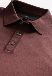 Burgundy polo shirt with a textured fabric, featuring a classic collar and three black buttons, labeled "NEXT" inside the collar.