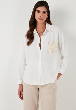 White button-down shirt with a textured, crocheted pocket detail and soft, lightweight fabric. Long sleeves and relaxed fit.