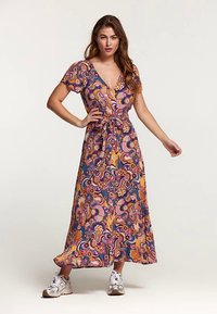 Abito lungo con stampa floreale paisley, caratterizzato da maniche corte, scollo a V e cintura annodata in vita. Indossato con scarpe da ginnastica argento.