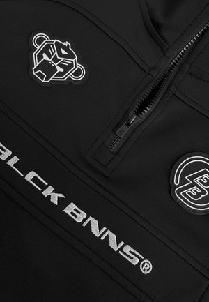 Zwart stoffen shirt met kwart-ritssluiting, ritssluiting, gestructureerde patches met een leeuwenlogo en merknaam in zilveren borduurwerk.