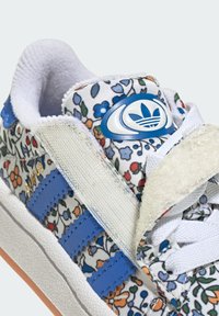 Floral-patterned sneakers with a white fabric upper, blue leather stripes, and a textured beige tongue logo. Rubber outsole with accent colors.