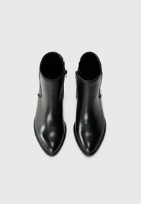 Botas de cuero negro hasta el tobillo con puntera puntiaguda, textura suave y cremalleras laterales. Diseño minimalista con bordes continuos y sin hardware visible.