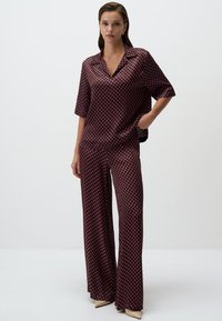Satin tweedelig outfit bestaande uit een kortemouwen top en wijde broek in een donker patroon van rode diamanten op een marineblauwe achtergrond.