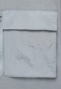 Lys grått stoff med en teksturert, krøllete finish; har en rektangulær lukkepose med en skjult glidelås på siden.