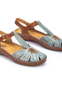 Sandalias de cuero azul claro con diseño floral perforado, detalles en cuero marrón y plantillas cómodas. Correa ajustable con costuras decorativas.