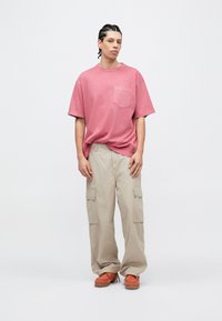 Ροζ βαμβακερό μπλουζάκι με κοντά μανίκια και τσέπη στο στήθος, συ�νδυασμένο με φαρδιά μπεζ παντελόνια cargo με πλαϊνές τσέπες και πορτοκαλί παπούτσια.