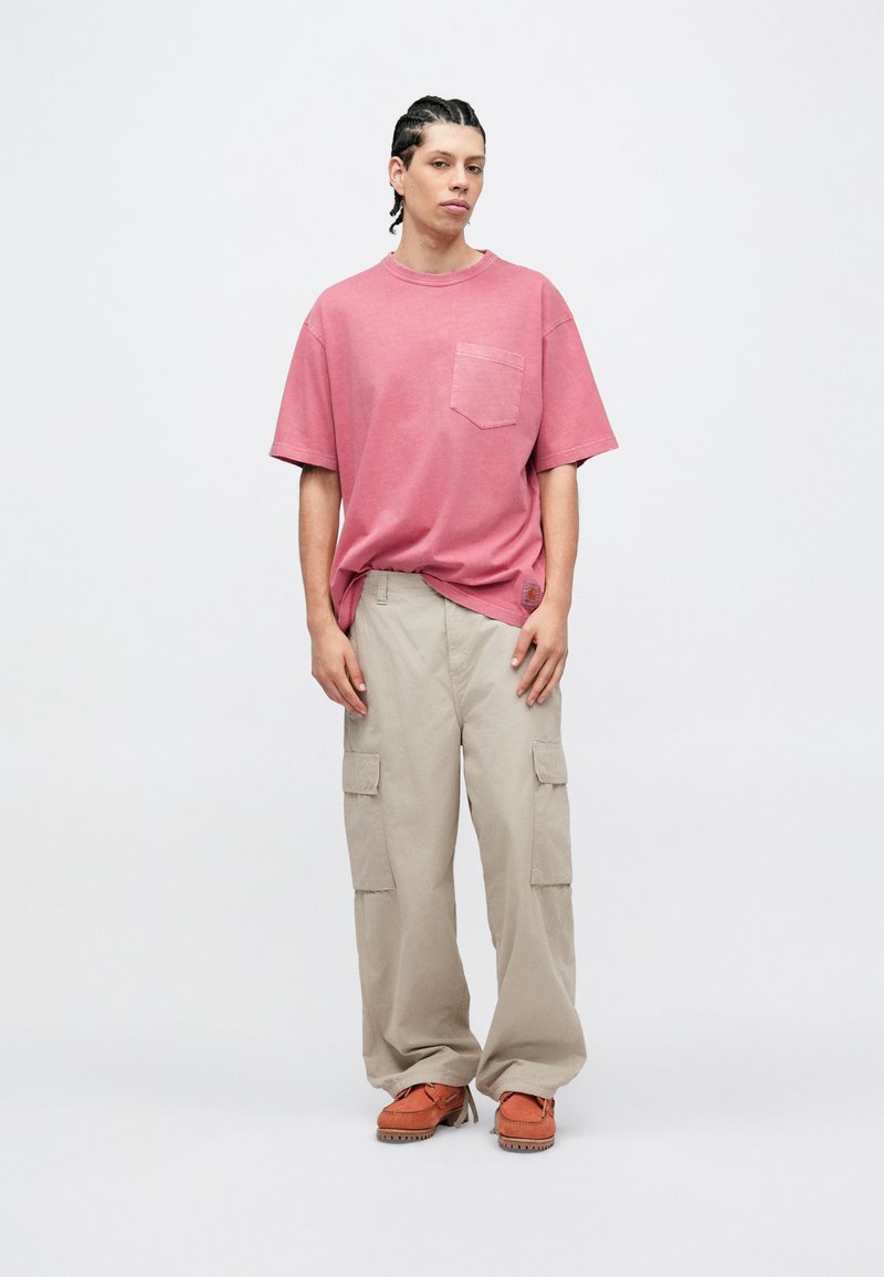 Kortærmet, lyserød bomulds T-shirt med brystlomme, kombineret med løstsiddende beige cargobukser med sidelommer og orange fodtøj.