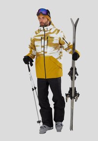 Skijakke i hvid med guld- og sorte mønstre, sorte bukser, handsker og skiudstyr. Har lynlåse og lommer. Lyse ski goggles.