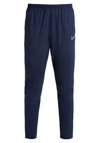 Mörkblå sportbyxor med elastisk midja, avsmalnande ben och en vit Nike-logotyp på övre vänstra sidan. Slät tygkänsla.