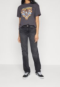 Camiseta gráfica gris con un diseño colorido de un águila, combinada con jeans de mezclilla oscura y zapatillas negras con acentos blancos.