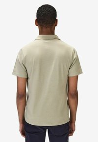 Piké i ljusbeige, kort ärm, kragdesign, mjuk textur, enkel bakvy, tillsammans med mörknavy byxor.