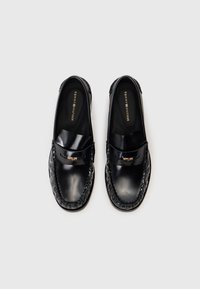 Černé kožené mokasíny s hladkým povrchem, pletenými švy a malým zlatým detailem na sponě. Klasický tvar a design.