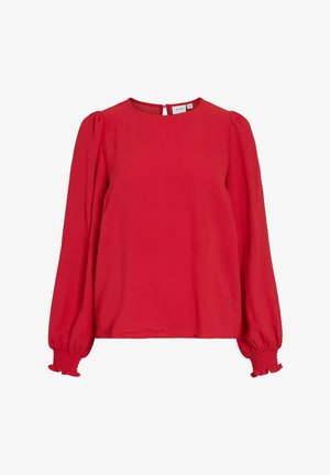 Blusa rossa a maniche lunghe con scollatura rotonda, tessuto testurizzato e maniche a sbuffo. I polsini presentano dettagli arricciati e una chiusura a oblò sul retro.