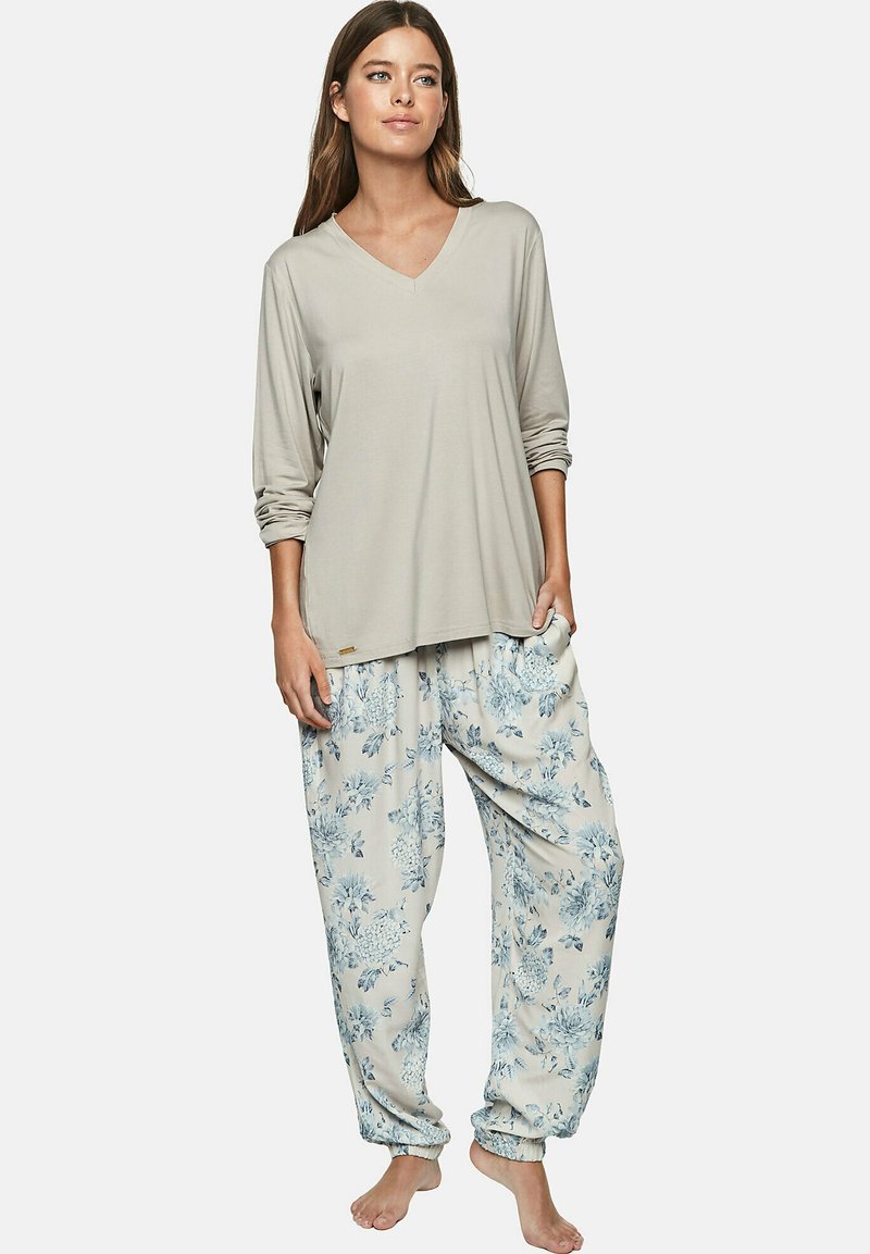 Haut gris clair à manches longues avec un col en V et des manches retroussées, associé à un pantalon beige à imprimé floral ample avec des poignets élastiques.