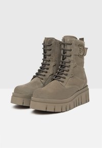 Bottes chevilles en daim souple de couleur vert olive chunky avec un laçage à l'avant, une fermeture éclair sur le côté et une semelle plateforme texturée. Présente des accents métalliques décoratifs.