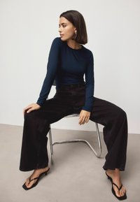 Navy long-sleeve fitted top paired with high-waisted black wide-leg jeans. Accessories include a metal ring and black flip-flop heeled sandals.