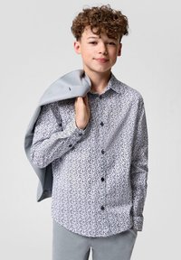 Witte shirt met een marineblauw abstract patroon, lange mouwen en knopen. Grijze blazer over de schouder gedrapeerd, met lichtgrijze broek.
