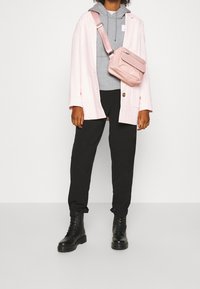 Blazer rosa sopra un hoodie grigio, pantaloni neri e stivali stringati neri; borsa a tracolla rosa con zip e dettaglio sulla tasca frontale.