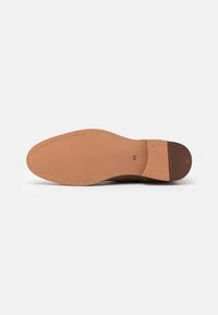Semelle en cuir de couleur beige avec une finition lisse. Présente un périmètre cousu assorti et une section de talon légèrement surélevée.