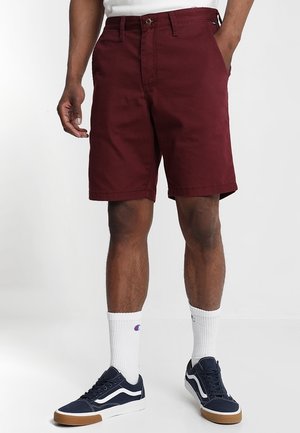 Pantaloncini bordeaux in cotone con fronte piatto, tasche laterali e chiusura con bottone. Abbinati a sneakers blu navy e calzini bianchi.