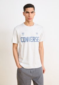 Hallhalli hall sinine "CONVERSE" tekst, trükitud keskelt. Omab ümmargust kaelust, lühikesi varrukaid ja logode detaile vasakul rinnal.