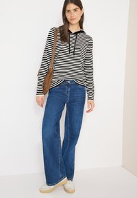 Zwart-wit gestreepte hoodie met capuchon, gecombineerd met wijde blauwe jeans. Het model draagt witte sneakers en een bruine crossbodytas.