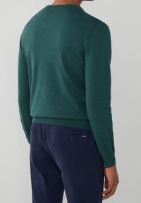 Pull vert tricoté avec un col rond et des manches longues, associé à un pantalon bleu marine doté d'une poche arrière avec un détail bouton.