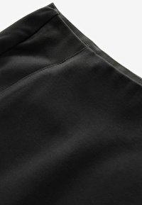 Tissu noir avec une texture lisse, présentant un léger éclat et un gros plan sur les coutures le long du bord.