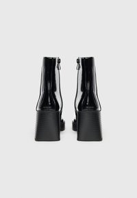 Bottes chelsea en cuir verni noir avec un talon bloc haut, présentant une texture lisse et une fermeture éclair à l'arrière.