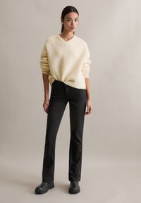 Kremowy, teksturowany sweter z dzianiny z dekoltem w serek, zestawiony z czarnymi dzwonowatymi jeansami i czarnymi botkami na masywnym obcasie.