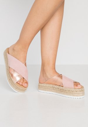 Sandales espadrilles à brides croisées roses avec un accent métallique et une semelle en jute, présentant un design à talon compensé et une semelle extérieure en caoutchouc blanc texturé.