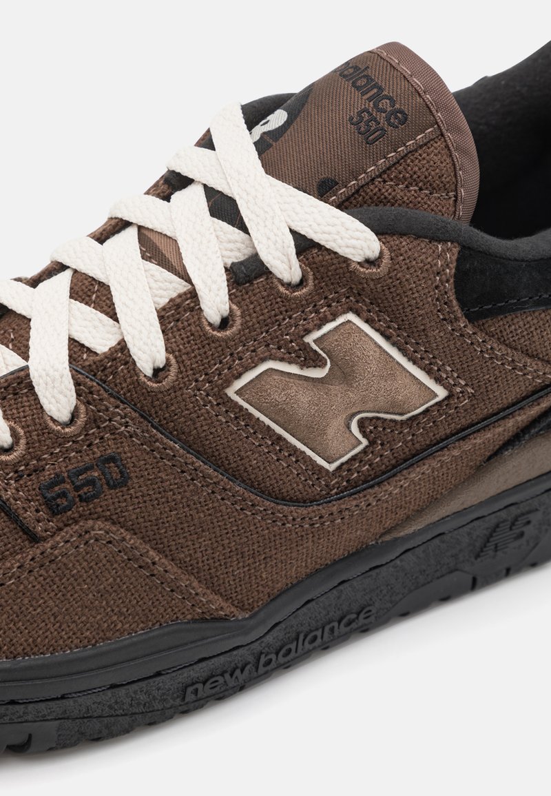 Zapatilla de lona marrón con suela de goma, cordones blancos, detalles en negro y un logo en el lateral. Número de modelo visible: 650.