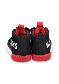 Baskets montantes noires avec des accents rouges, présentant un tissu texturé et une semelle en caoutchouc blanche. Logo "BOSS" affiché en évidence sur les côtés.