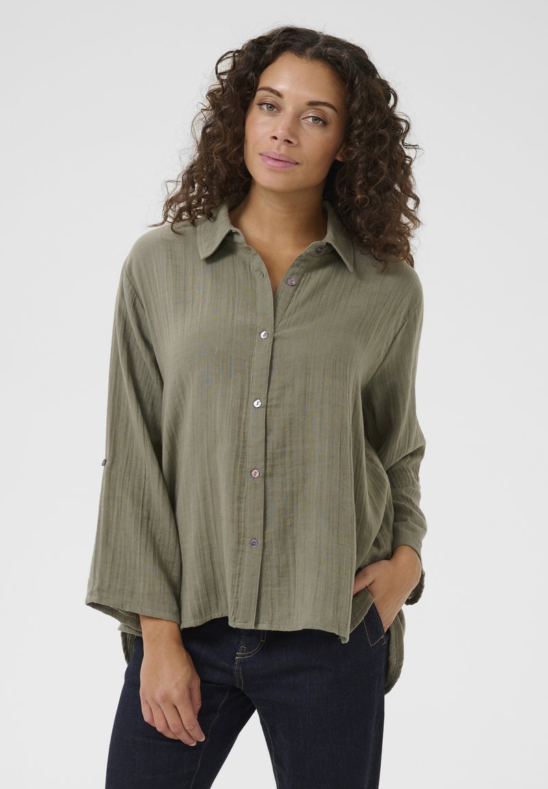 Olive green, button-up shirt with a collar, long sleeves, and a relaxed fit. Textured fabric with subtle stripes and purple buttons.